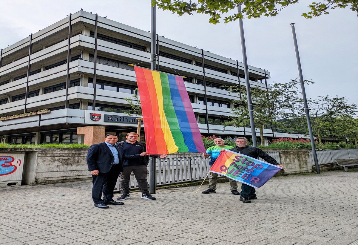 Bürgermeister Christian Vogt, Sven Rühl, Kai Grosser und Hermann mit ehisster Regenbogenfahne vor dem Rathaus